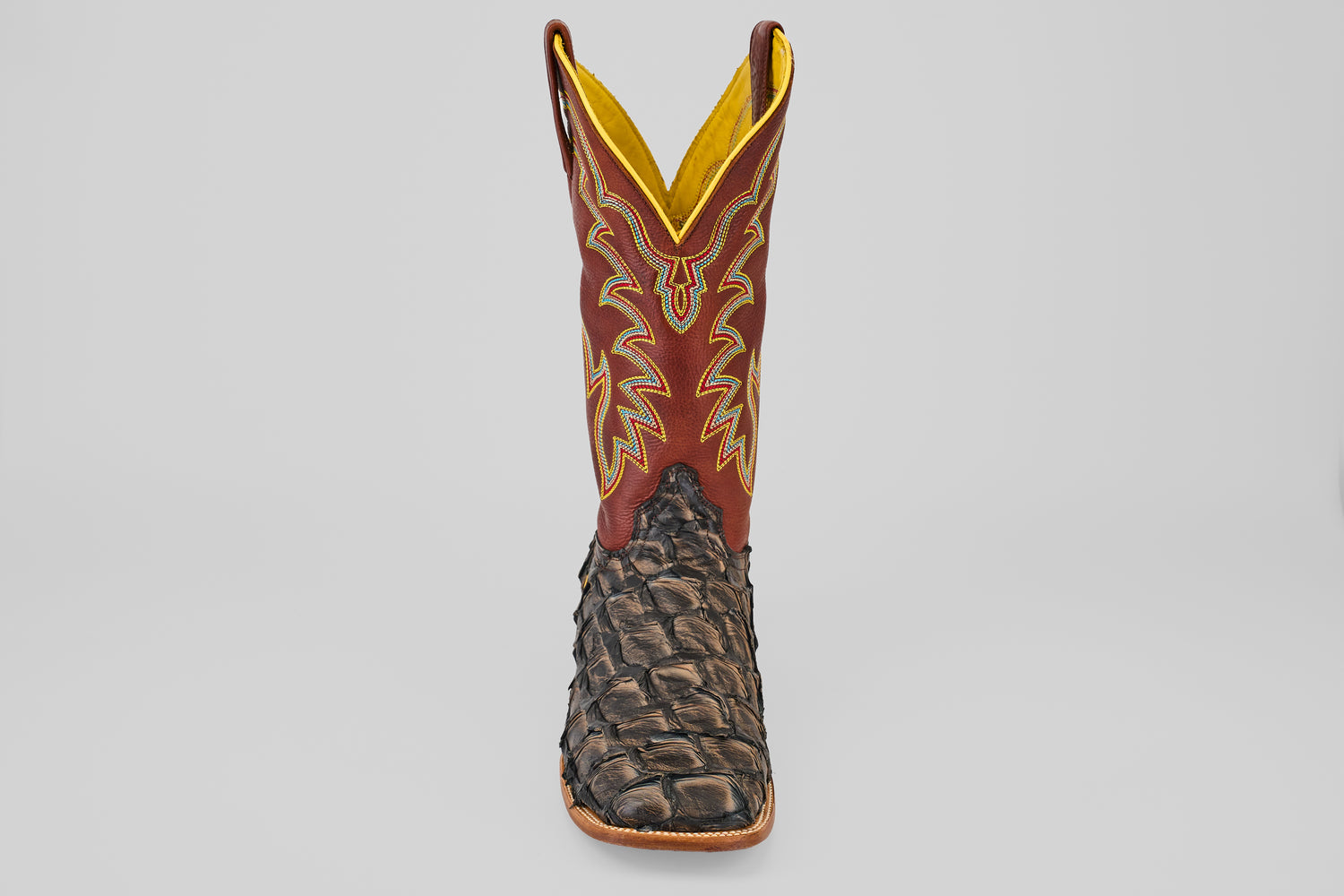 A single Butch - Caramel - Square Toe cowboy boot with a textured dark brown Pirarucu leather foot and a tall red shaft featuring yellow and beige stitching, viewed from the front against a plain light background.