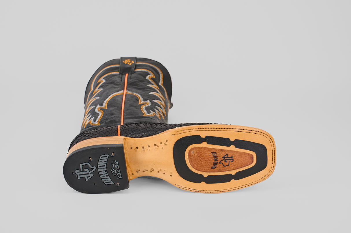 A Wayne - Matte Black - Square Toe boot with tan decorative stitching is shown on its side, revealing the DIAMOND-branded sole. The boot features intricate patterns, a textured heel, and signature western style.