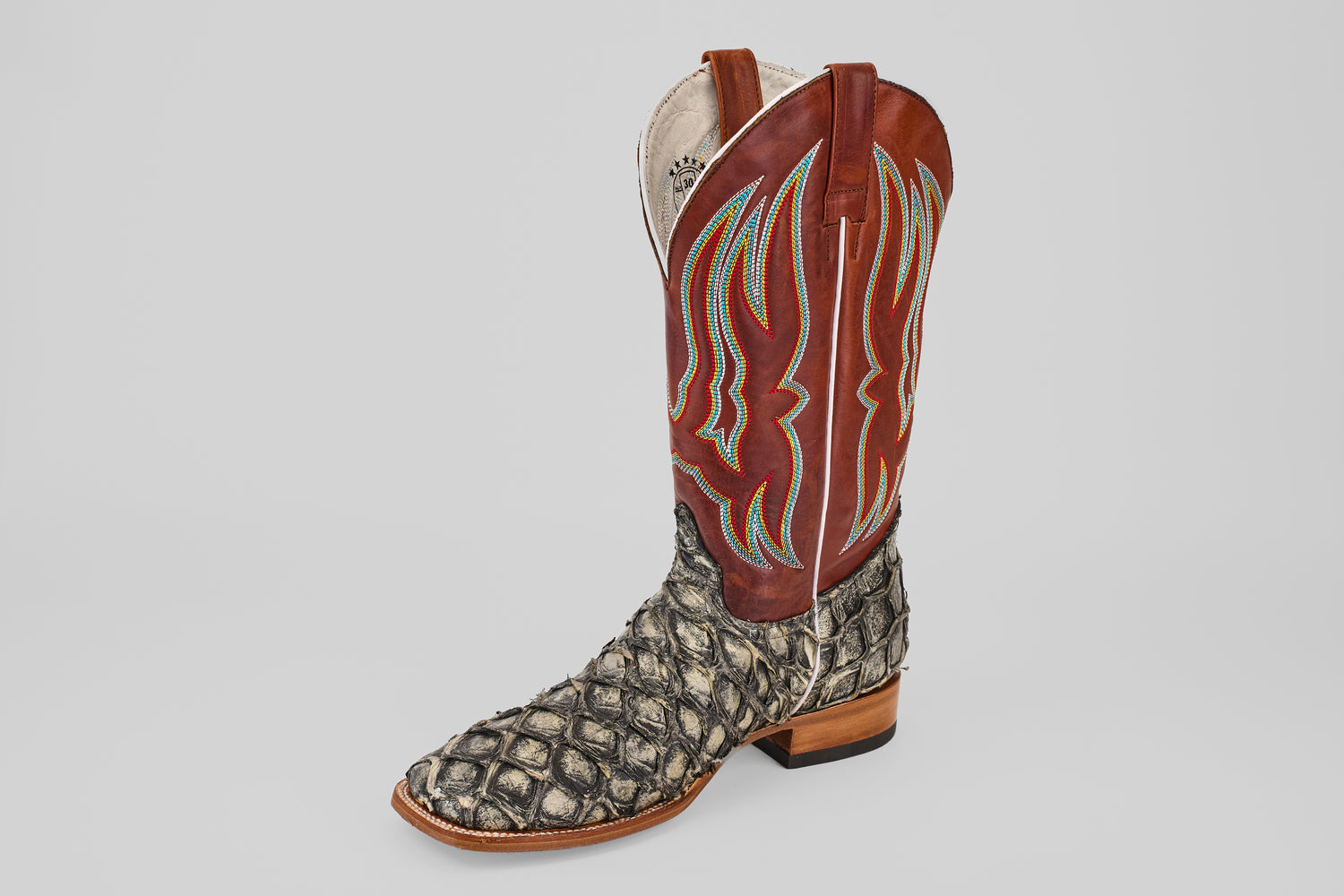 The Robinson - Newspaper - Square Toe is a limited edition cowboy boot featuring a textured black and white Purarucu leather lower, tall brown upper, and blue and yellow decorative stitching—expertly crafted.