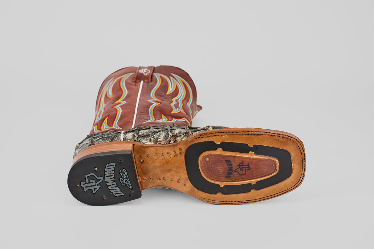 The Robinson - Newspaper - Square Toe boot is shown on its side, revealing a leather sole with black rubber grip, a handcrafted scale-textured Purarucu leather lower, and a brown upper accented by red and yellow stitching.