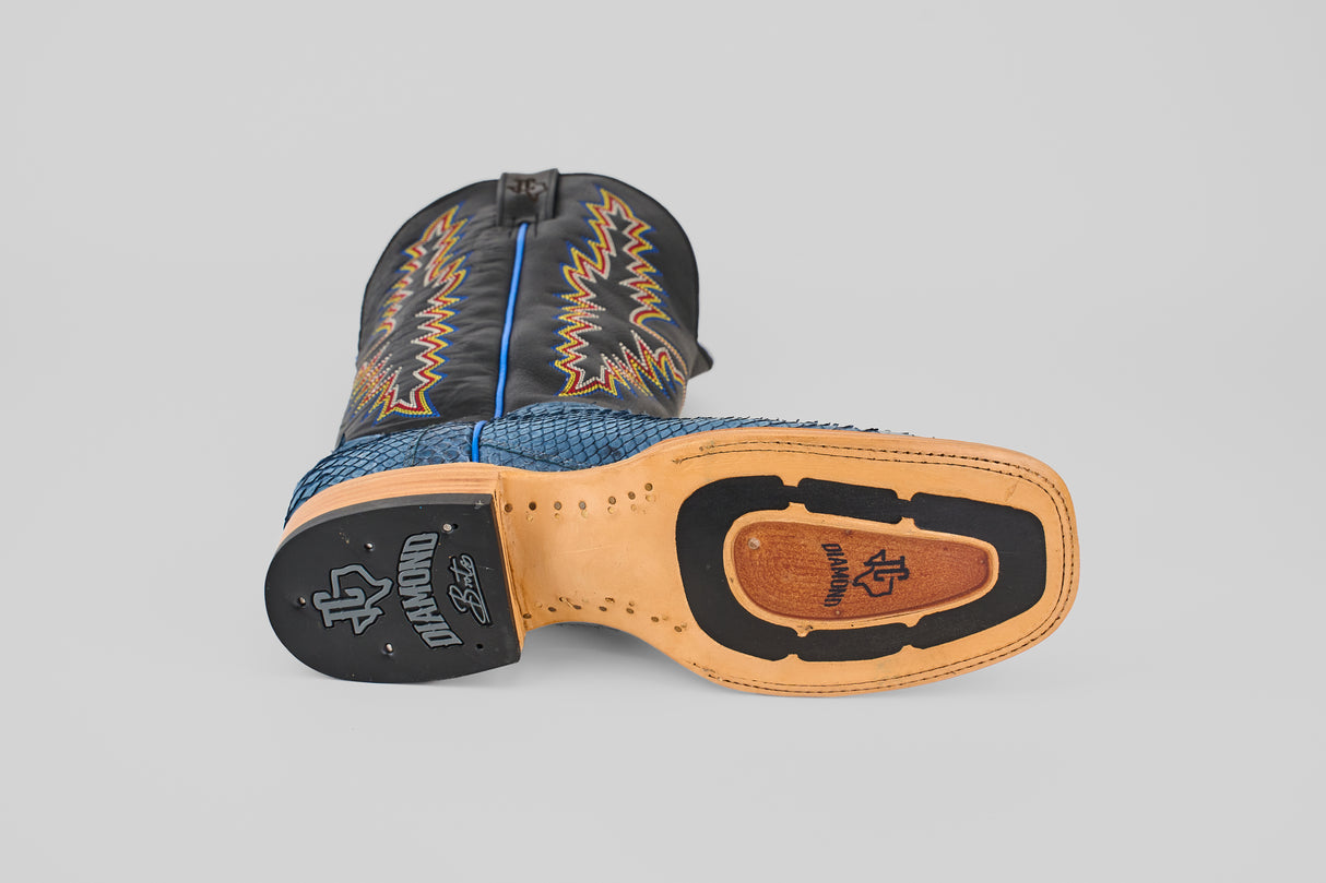 The Kingsley - Blue Jeans - Square Toe boot from the Diamond Collection lies on its side, displaying a tan and black sole with decorative stitching. Its black leather upper features blue and orange zigzag accents—ideal for any occasion.