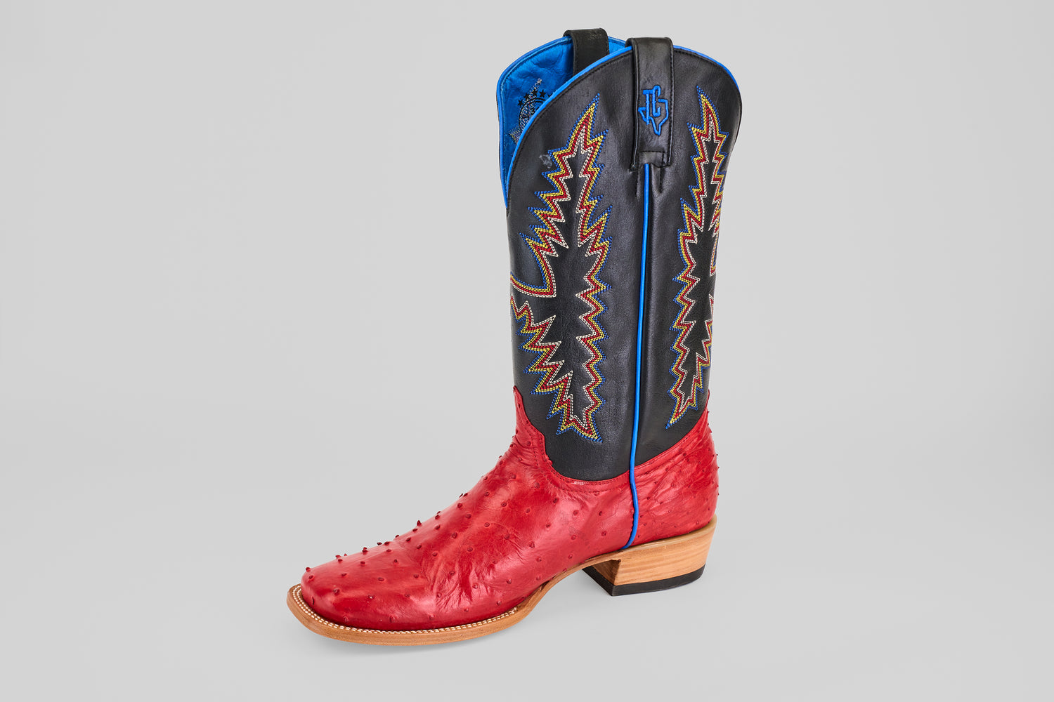 The Crowley - Red - Square Toe cowboy boot features a red ostrich leather foot, black shaft with colorful zigzag stitching, blue trim, and a wooden heel. Displayed on a plain light gray background.