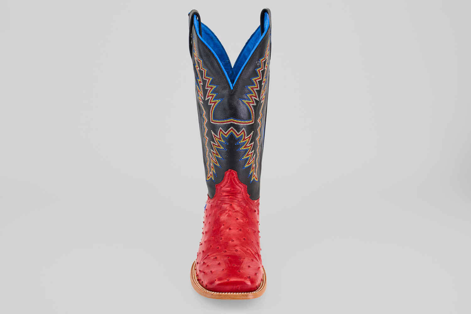 The Crowley - Red - Square Toe boot features a red leather foot, a black and blue shaft with yellow and blue stitching, and is displayed upright against a gray background.
