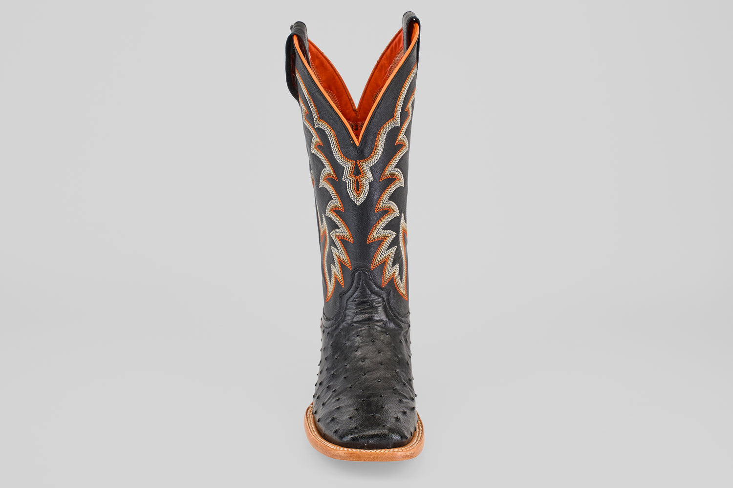 The Steele - Black - Square Toe boot features textured leather, a black square toe, intricate orange and grey stitching, and a brown sole, presented front view against a light gray background—ideal for luxury footwear seekers.