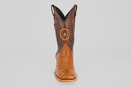 The Exotic Full Quilt Ostrich - Brandy Brucciato, a single square toe cowboy boot in rich brown with a decorative star emblem on the front, is displayed upright against a plain light gray background.