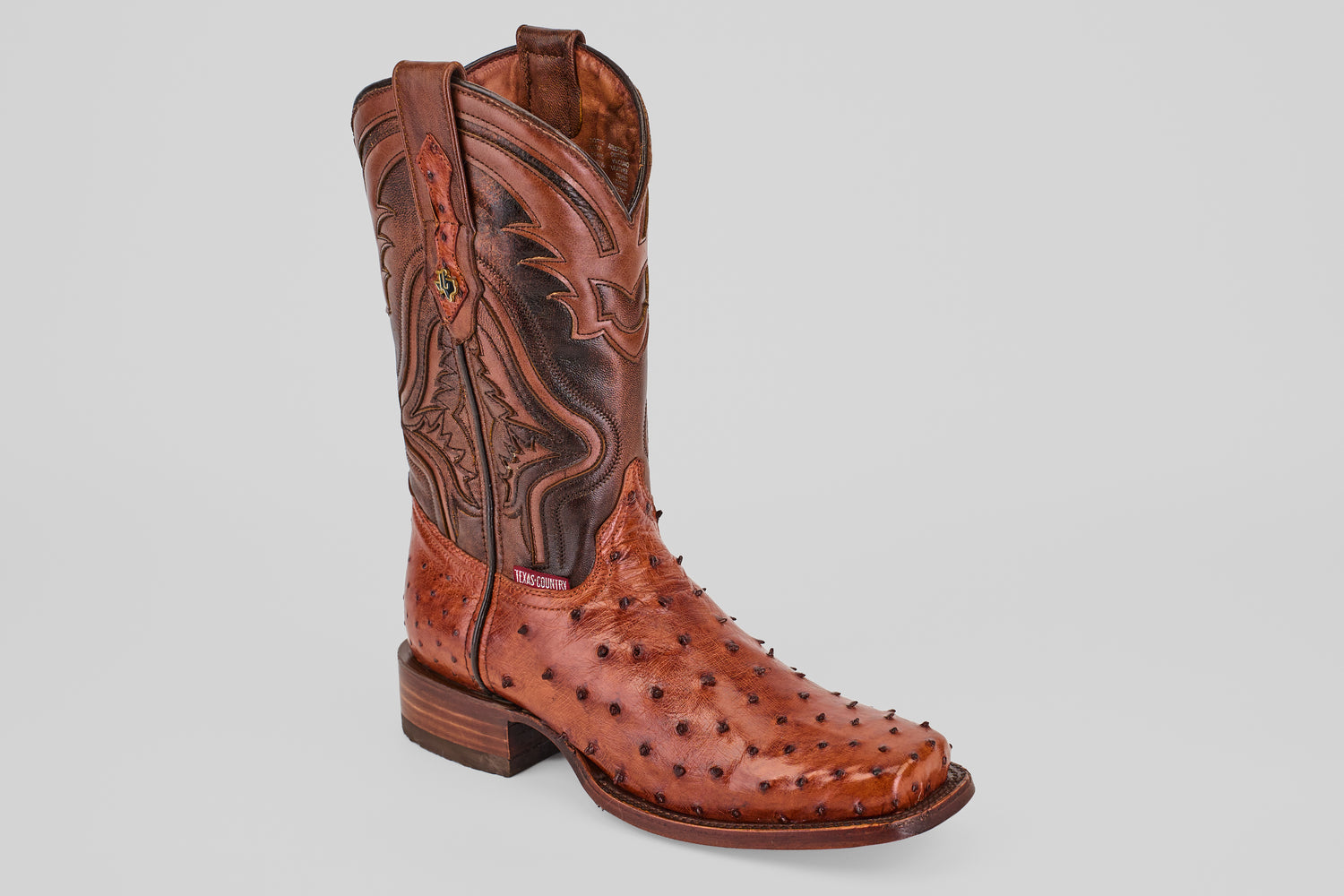 A single Exotic Ostrich - Brandy - Rodeo Toe boot, crafted from genuine ostrich leather with decorative stitching and textured bumps, pointed toe, low heel, and pull straps, shown on a plain light gray background.