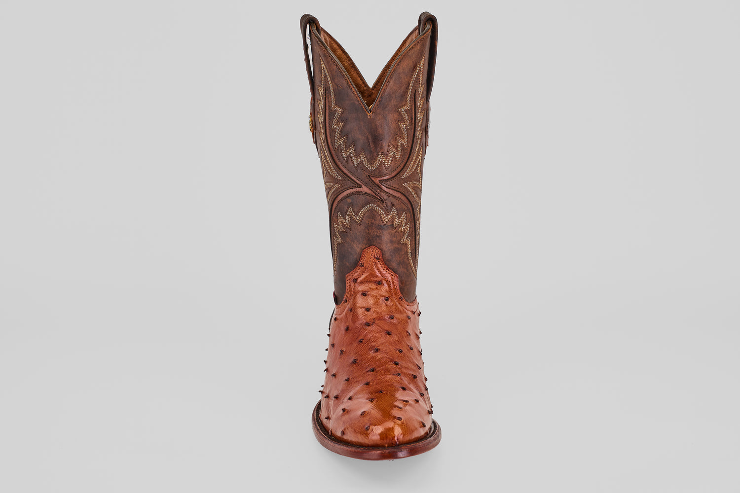 A single Exotic Full Quilt Ostrich - Brandy - Round Toe cowboy boot in brown, handcrafted with decorative stitching and a shiny quilted ostrich leather finish, shown from the front against a plain light background.