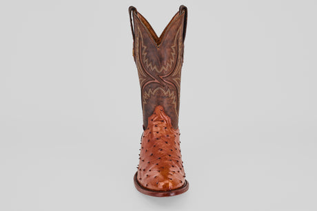 A single Exotic Full Quilt Ostrich - Brandy - Round Toe cowboy boot in brown, handcrafted with decorative stitching and a shiny quilted ostrich leather finish, shown from the front against a plain light background.