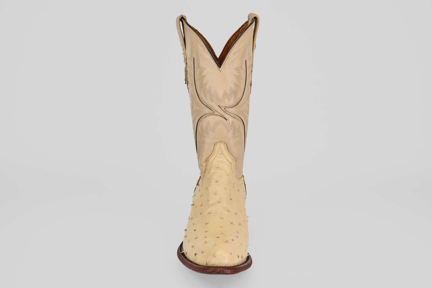 The Exotic Full Quilt Ostrich - Bone features a single genuine ostrich leather cowboy boot in beige with a round toe, decorative shaft stitching, and dark brown sole, displayed facing forward on a plain light background.