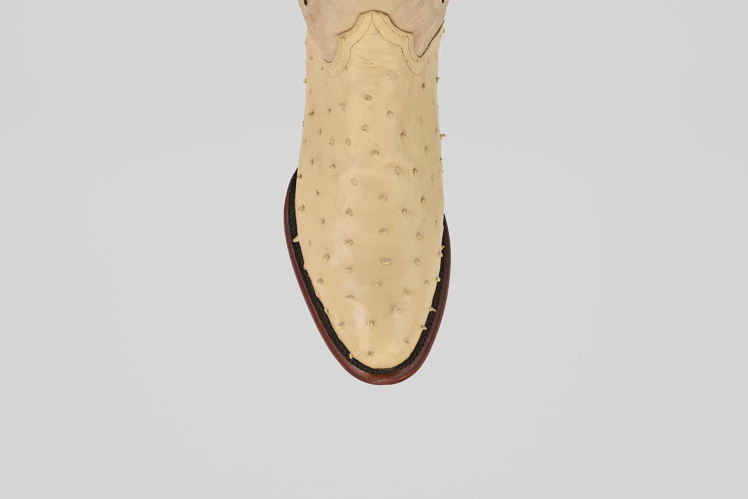 A top-down view of the Exotic Full Quilt Ostrich - Bone - Round Toe cowboy boot’s toe, featuring beige genuine ostrich leather and a brown sole, showcases its luxurious texture and craftsmanship against a white background.