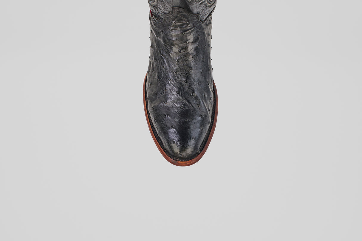A top-view close-up of the Exotic Full Quilt Ostrich - Black - Round Toe boot, featuring textured black ostrich leather and a brown sole against a white background, highlights its classic Western style.