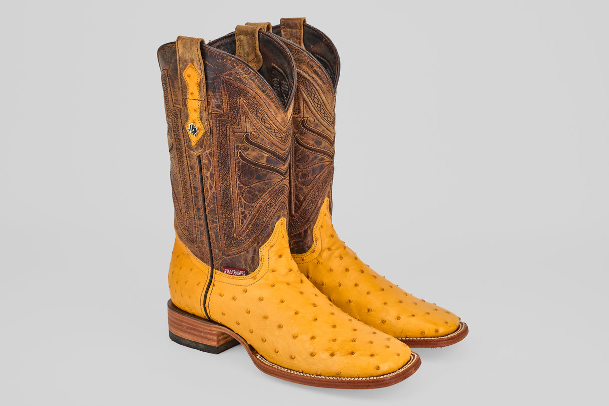 The Exotic Full Quilt Ostrich - Buttercup- Square Toe boots feature a light brown ostrich leather foot, darker tooled shafts, and wooden heels, displayed against a plain light gray background.
