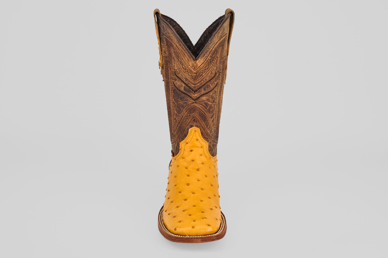 The Exotic Full Quilt Ostrich - Buttercup- Square Toe features a yellow ostrich leather foot and a tall, brown, intricately stitched shaft—shown facing forward on a plain gray background—for handcrafted western boot enthusiasts.