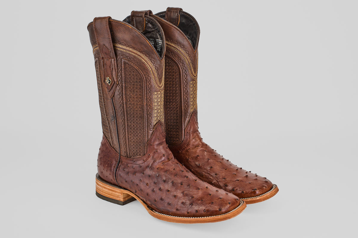 The Exotic Full Quilt Ostrich - Brown - Square Toe boots feature textured ostrich leather, decorative shaft stitching, and light wooden heels, displayed against a plain gray background.