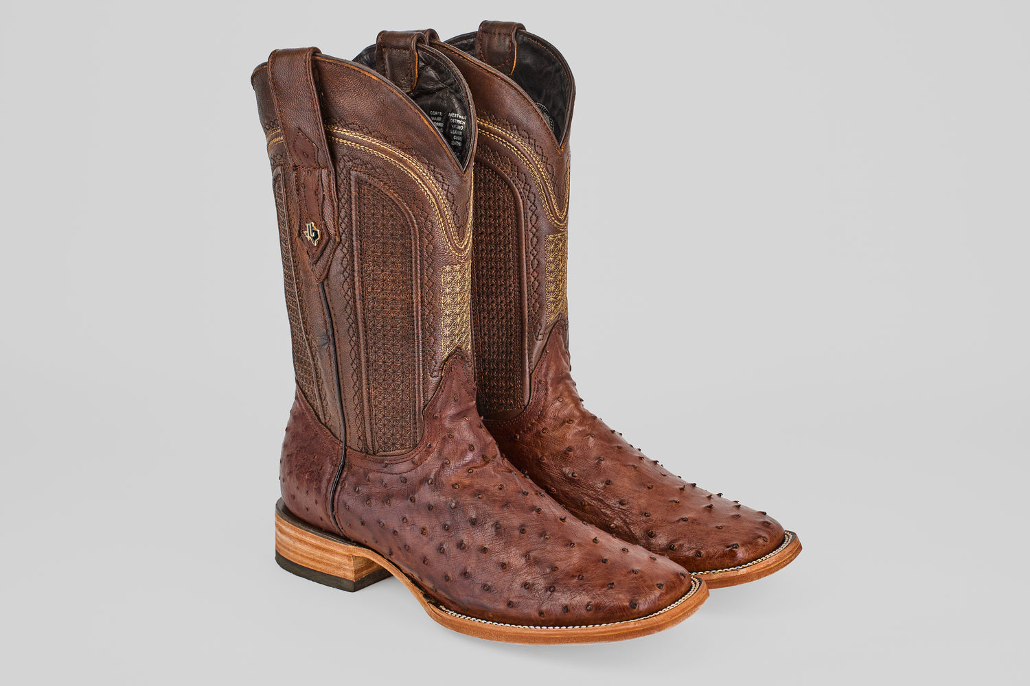The Exotic Full Quilt Ostrich - Brown - Square Toe boots feature textured ostrich leather, decorative shaft stitching, and light wooden heels, displayed against a plain gray background.