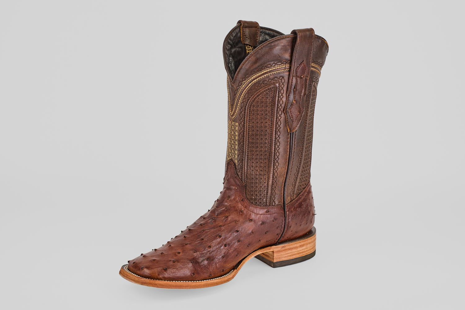 The Exotic Full Quilt Ostrich boot in brown features textured leather, decorative stitching, a wooden heel, and a classic square toe, displayed against a plain light gray background.