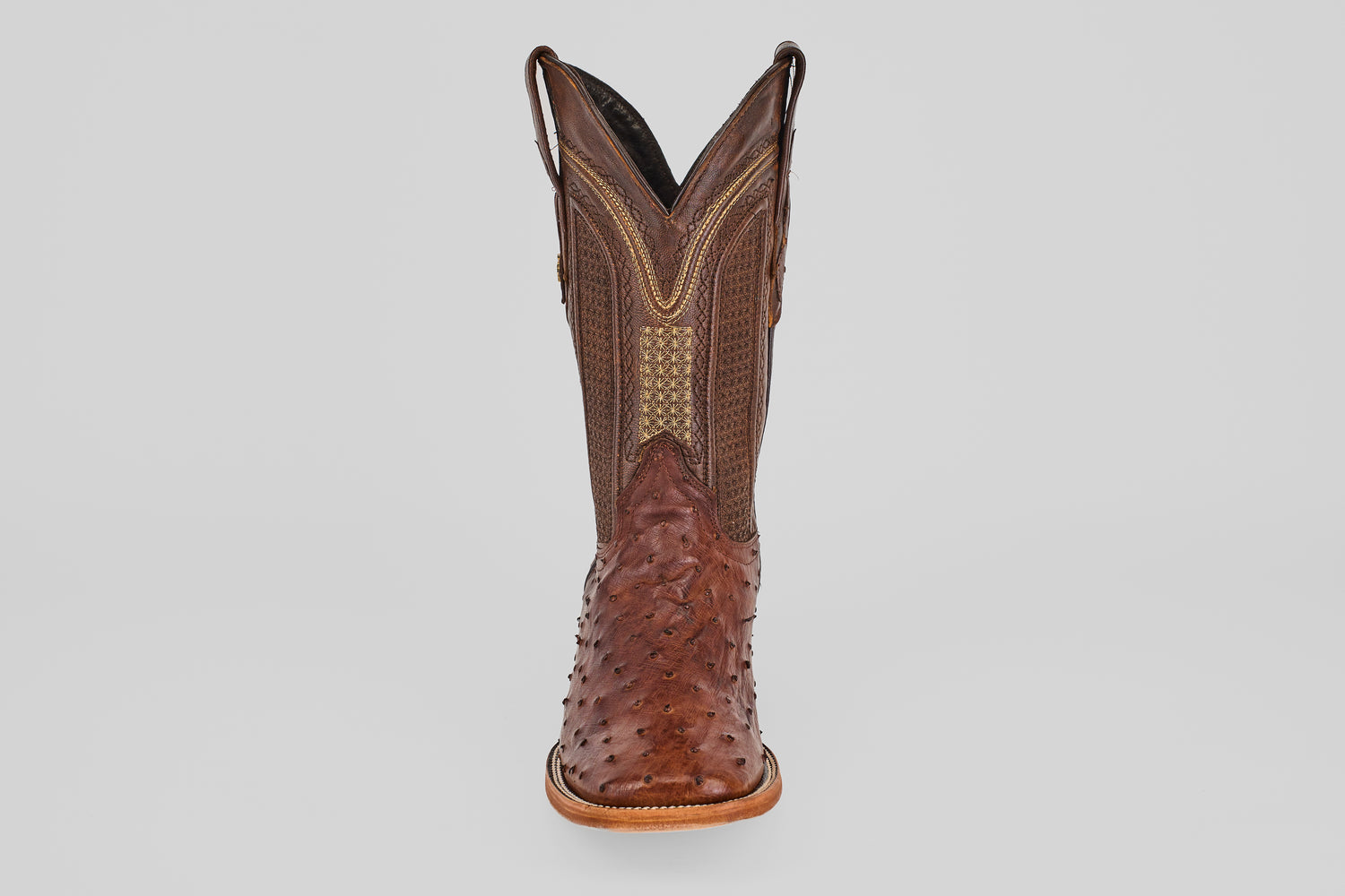 A single Exotic Full Quilt Ostrich - Brown - Square Toe boot made of textured leather with intricate stitching and a patterned toe and shaft, reminiscent of ostrich boots, is shown from the front against a plain light background.