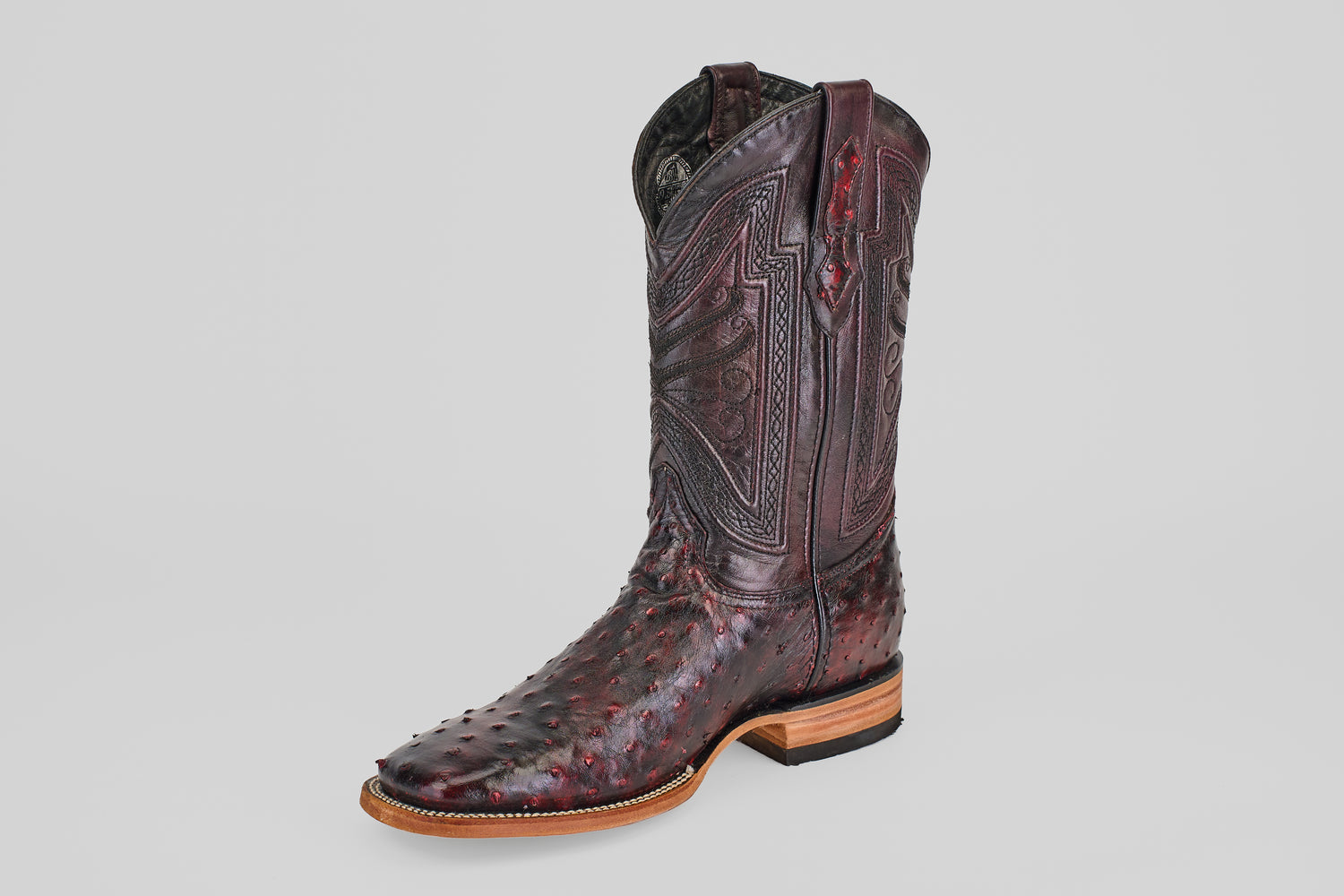 A single Exotic Full Quilt Ostrich boot in Black Cherry with a square toe, featuring intricate shaft stitching and textured ostrich leather, is displayed on a plain gray background.