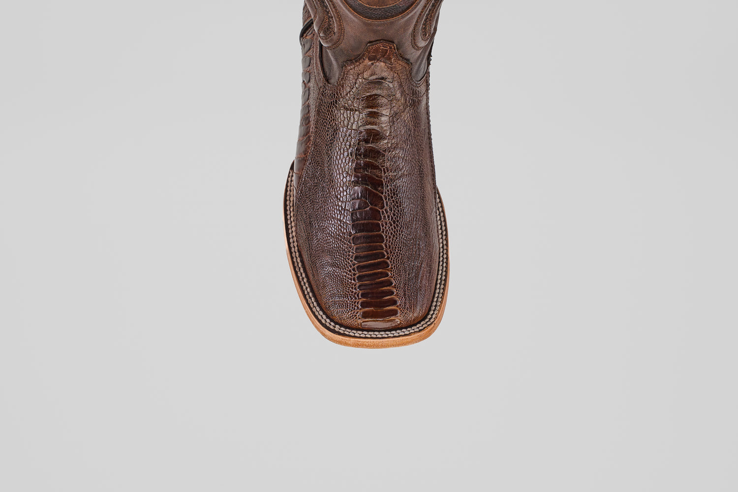 A close-up of the toe on the Austin Leg - Brown - Square Toe cowboy boot, featuring textured ostrich leather and detailed stitching, set against a plain light gray background.