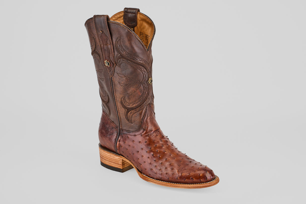 The Austin - Tabaco - Roper Toe is a single brown men's cowboy boot with decorative stitching and a textured ostrich leather pattern, featuring a stacked wooden heel and roper toe, displayed on a light gray background.