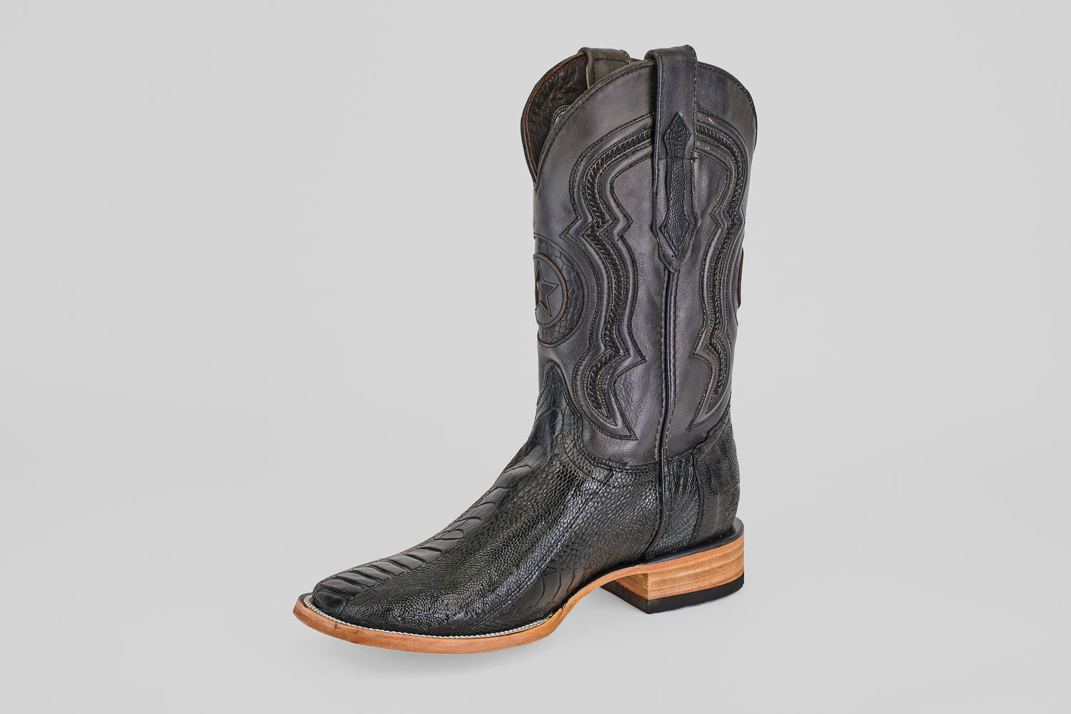 The Austin Leg - Black - Square Toe is a single black cowboy boot with decorative stitching, a square toe, and a light brown wooden heel, displayed on a plain light gray background. Ideal for fans of classic cowboy boot style.