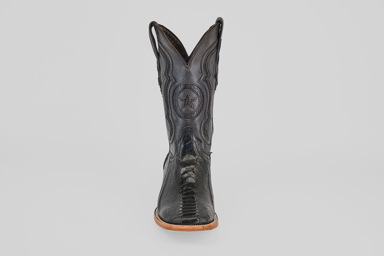 The Austin Leg - Black - Square Toe boot features decorative stitching, a star emblem on the shaft, and a light tan sole. Photographed from the front on a plain light gray background, it's ideal for square toe boot enthusiasts.