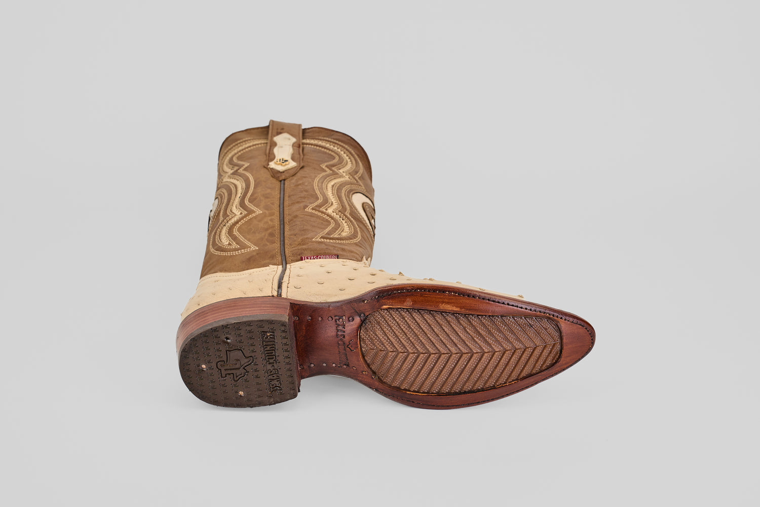 The Austin - Bone - Snip Toe boots feature classic western style with detailed stitching, textured leather, and a durable rubber sole—one boot stands upright while the other lies on its side to showcase their craftsmanship.