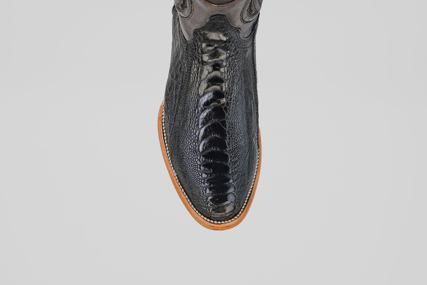 Overhead view of the Austin Leg - Black - Roper Toe boot featuring shiny black ostrich leather with a textured finish and a light brown sole, displayed on a plain light gray background.