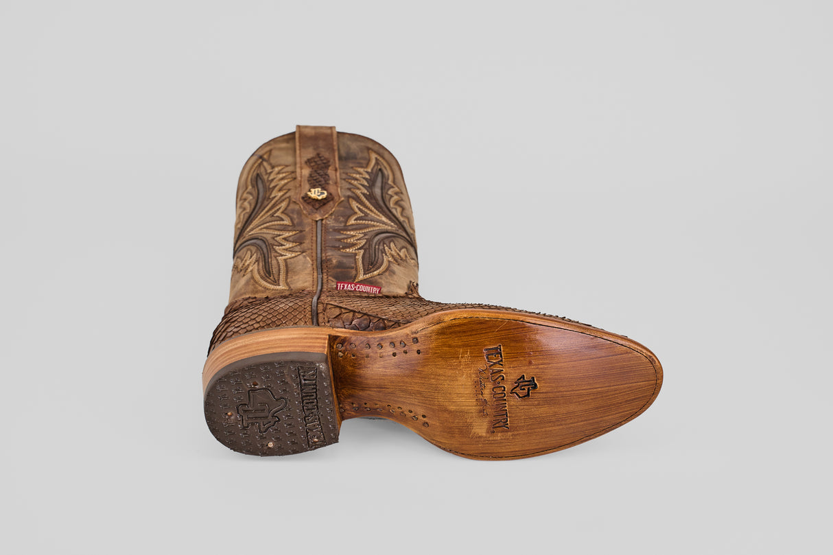 The Tanner - Tamarindo - Round Toe boots in brown Python are shown: one upright, one on its side displaying the TEJANOS COWBOY sole. They have decorative stitching and textured detailing on the lower part.