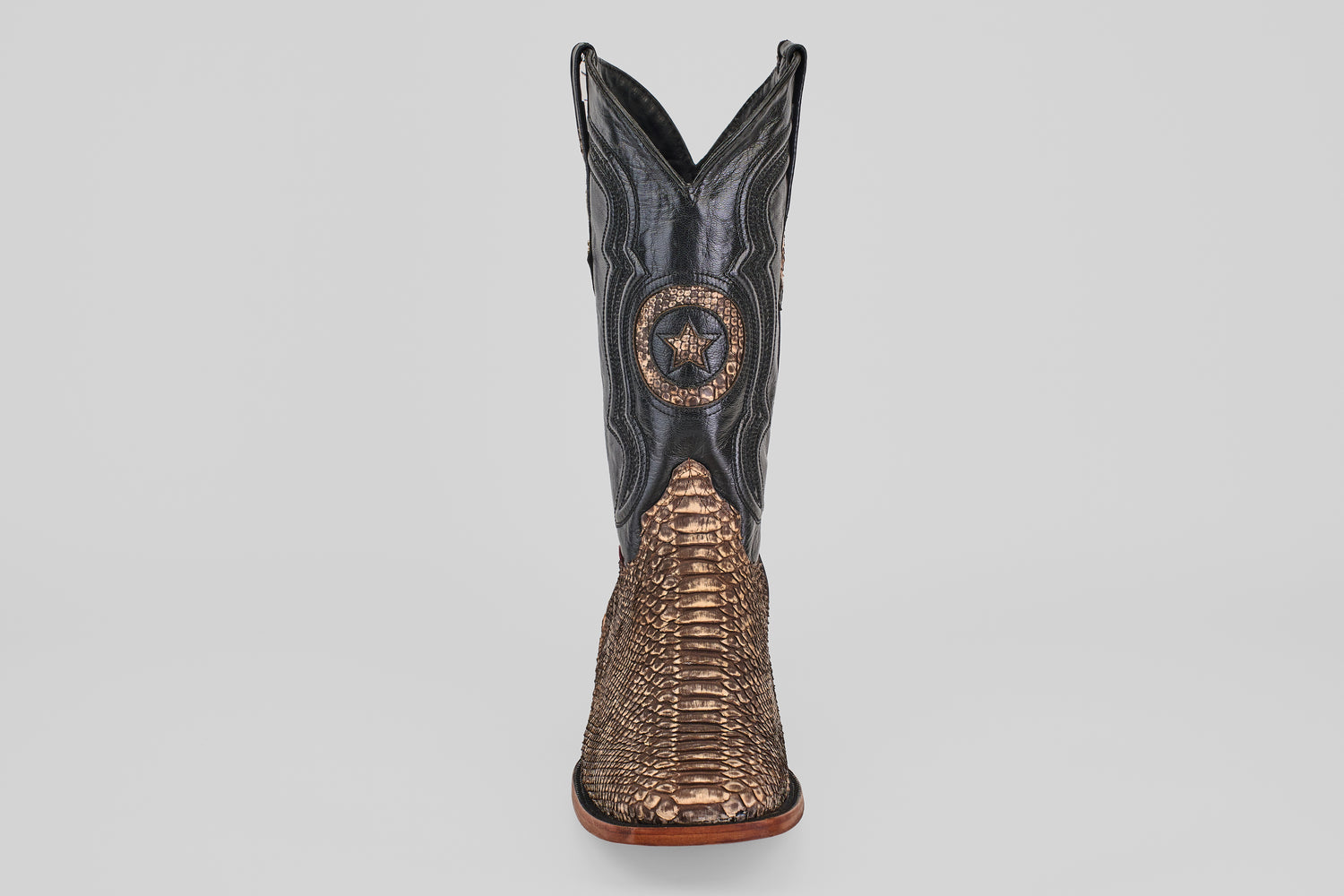 The Tanner - Rustic Bone - Square Toe cowboy boot features a brown snakeskin-textured lower, black upper shaft, and a decorative star emblem on the front—reflecting Western craftsmanship and the allure of exotic leather.
