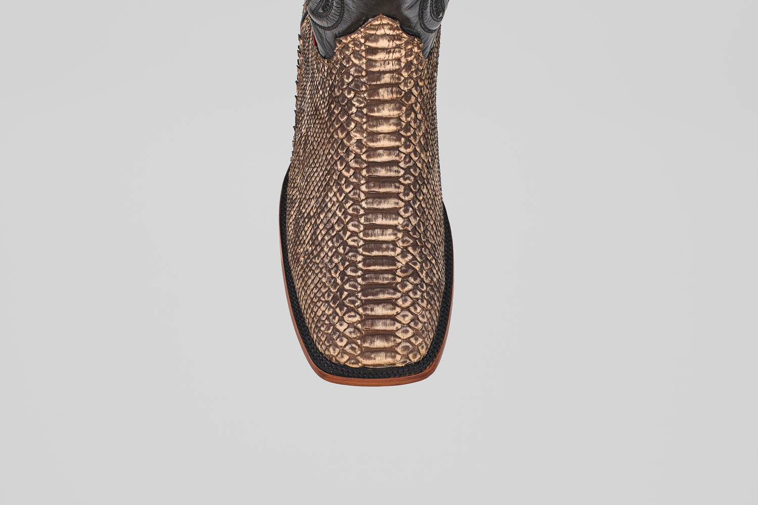 A close-up top view of the Tanner - Rustic Bone - Square Toe boot, featuring brown textured python snakeskin and a square toe, highlights its exotic leather and Western craftsmanship on a light gray background.