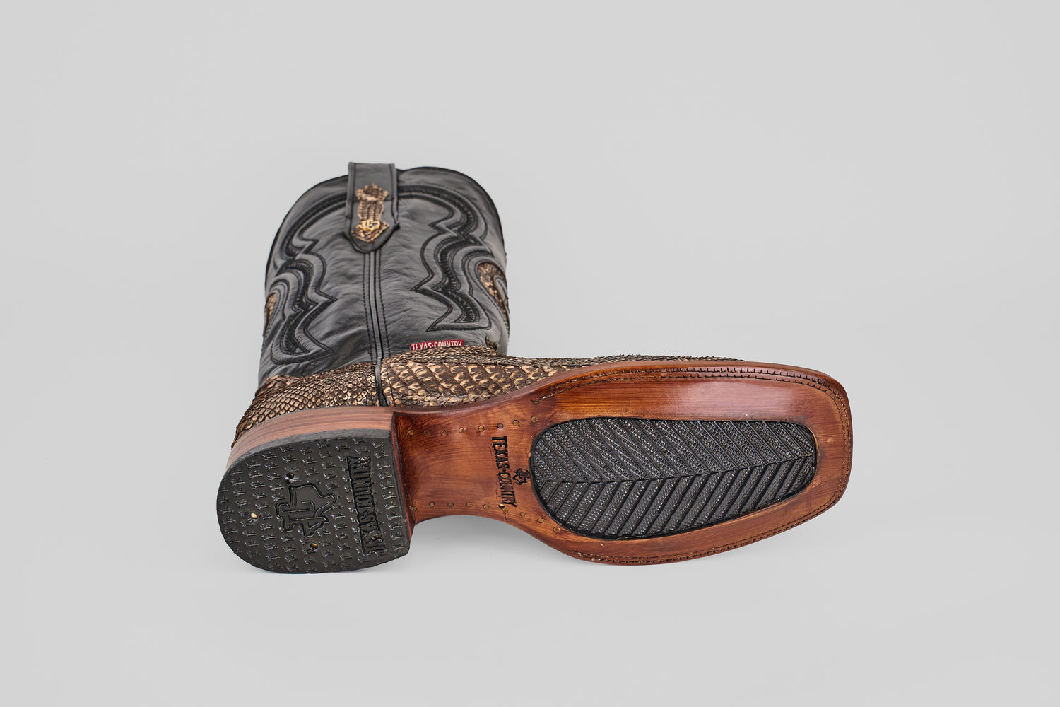 The Tanner - Rustic Bone - Square Toe cowboy boots feature textured tan exotic leather, black shafts, and a brown leather-rubber sole with detailed stitching and embossed branding, capturing authentic Western craftsmanship.