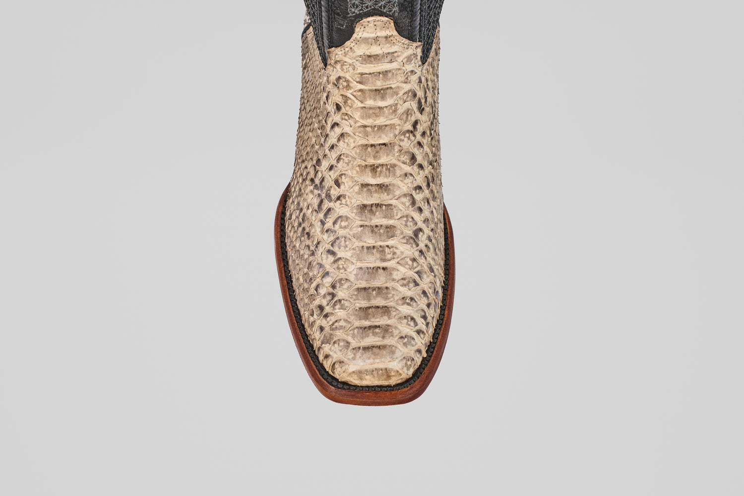 A close-up, top-down view of the Tanner - Natural - Narrow Square Toe boot displays its light python-textured snakeskin and dark upper, highlighting distinct Western style against a plain white background.