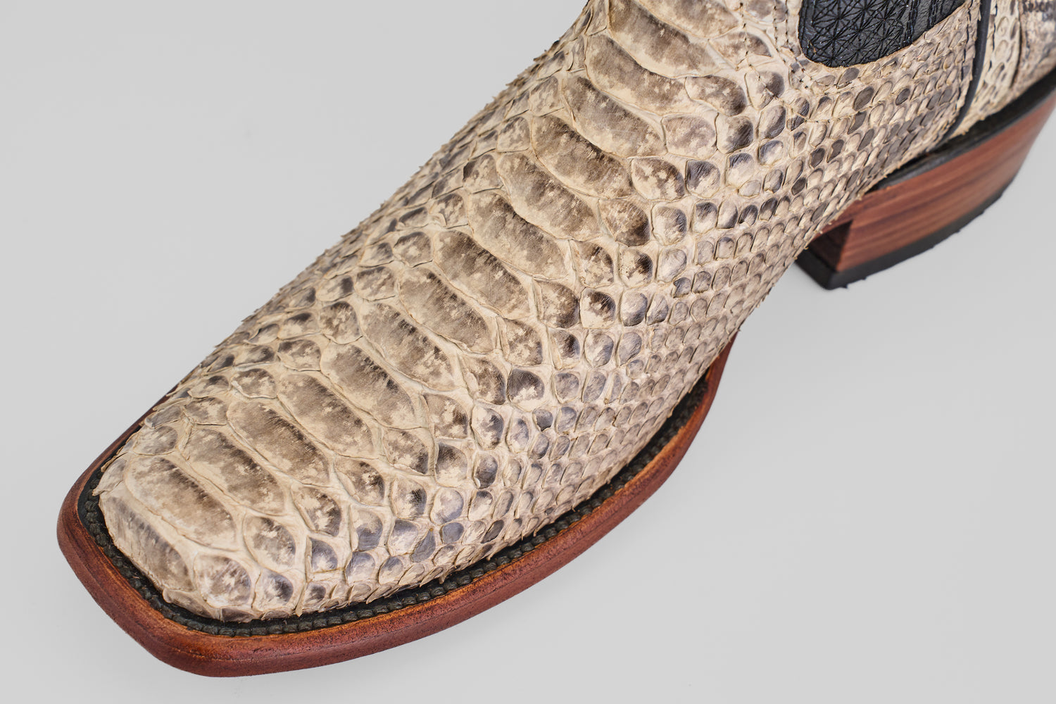Close-up of the Tanner - Natural boots, crafted in beige python leather with a narrow square toe, showcasing detailed texture, a wooden sole, and black stitching.