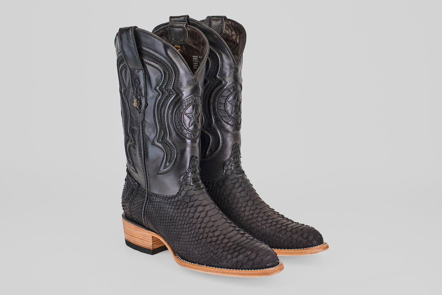 The Tanner – Matte Black – Roper Toe boots feature black, textured snakeskin-like leather, intricate shaft stitching, and light brown wooden heels and soles, shown against a plain gray background.