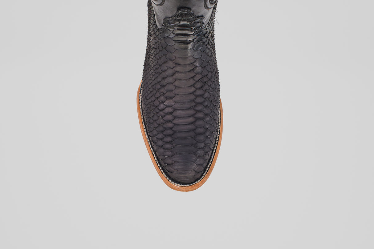 A top-down view of the Tanner – Matte Black – Roper Toe boot, featuring matte black python leather and a light brown sole, displayed on a plain white background.