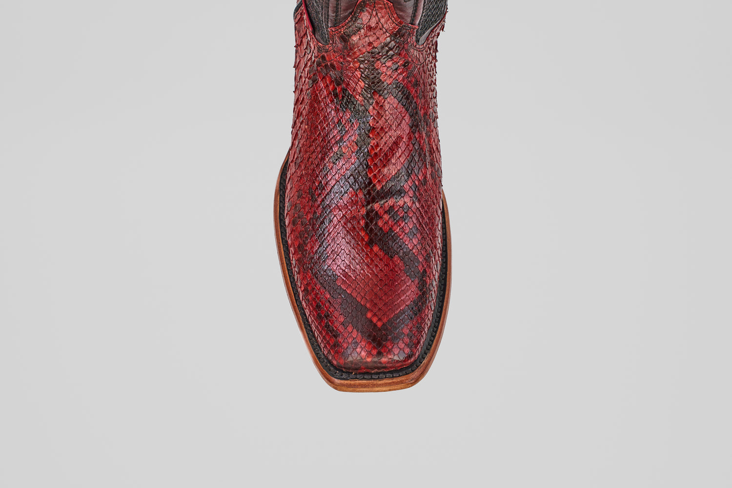 A close-up top view of the Tanner – Ruby – Narrow Square Toe, a red Python leather cowboy boot with a brown sole, set against a plain white background.