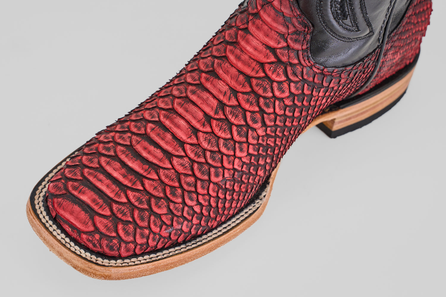 A close-up of the Tanner – Scarlet – Square Toe cowboy boot, featuring red python leather, black accents, and a tan wooden heel and sole, displayed against a plain light background.
