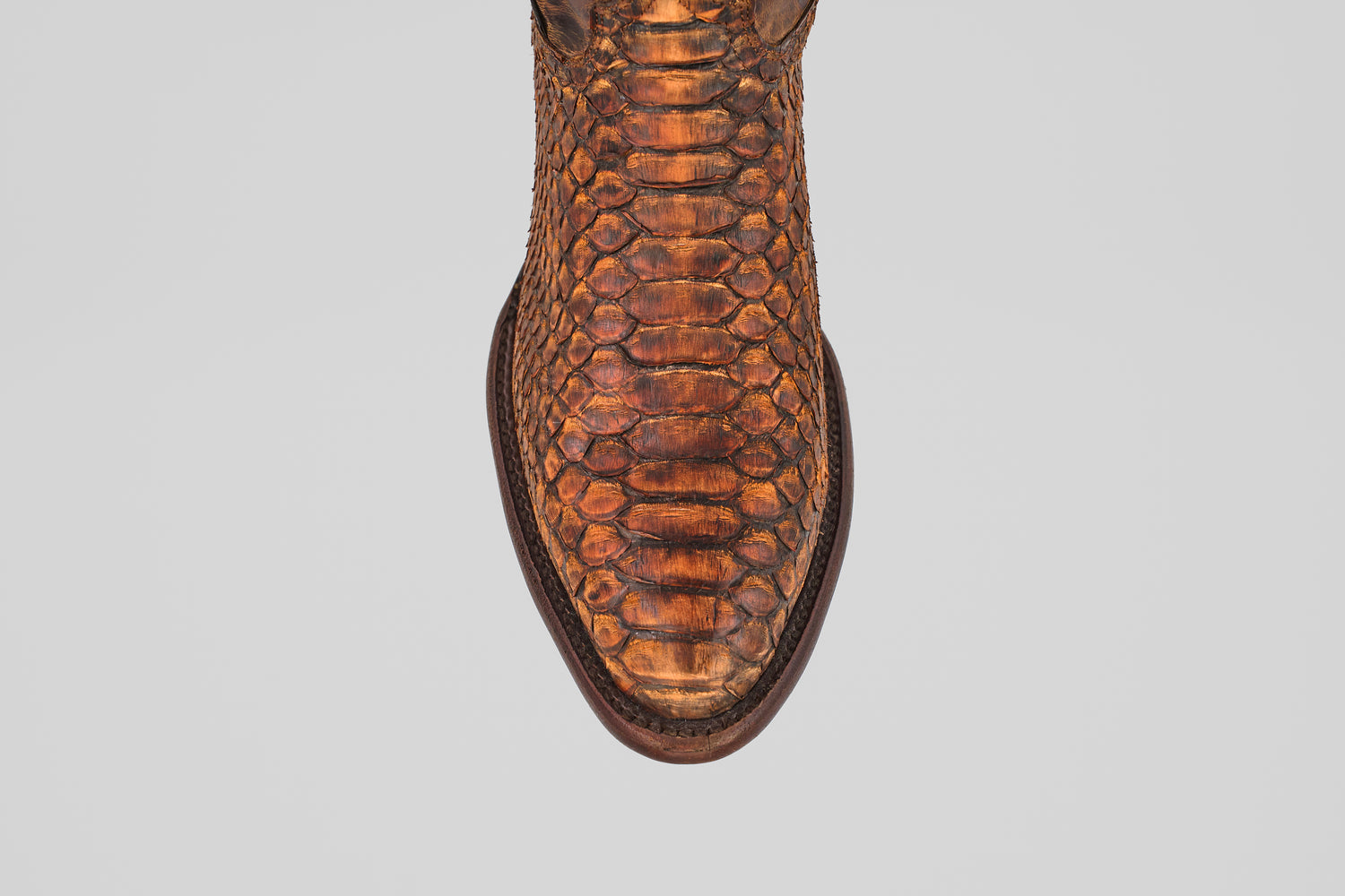 A top-down view of the Tanner – Chestnut – Round Toe boot, showcasing its brown python leather, detailed scale pattern, and dark brown trim around the sole—an ideal choice for western fashion enthusiasts.