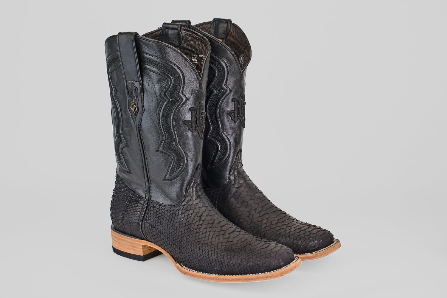 A pair of Tanner - Matte Black - Square Toe boots with textured, scaly leather and light tan wooden soles, standing side by side on a plain light gray background.