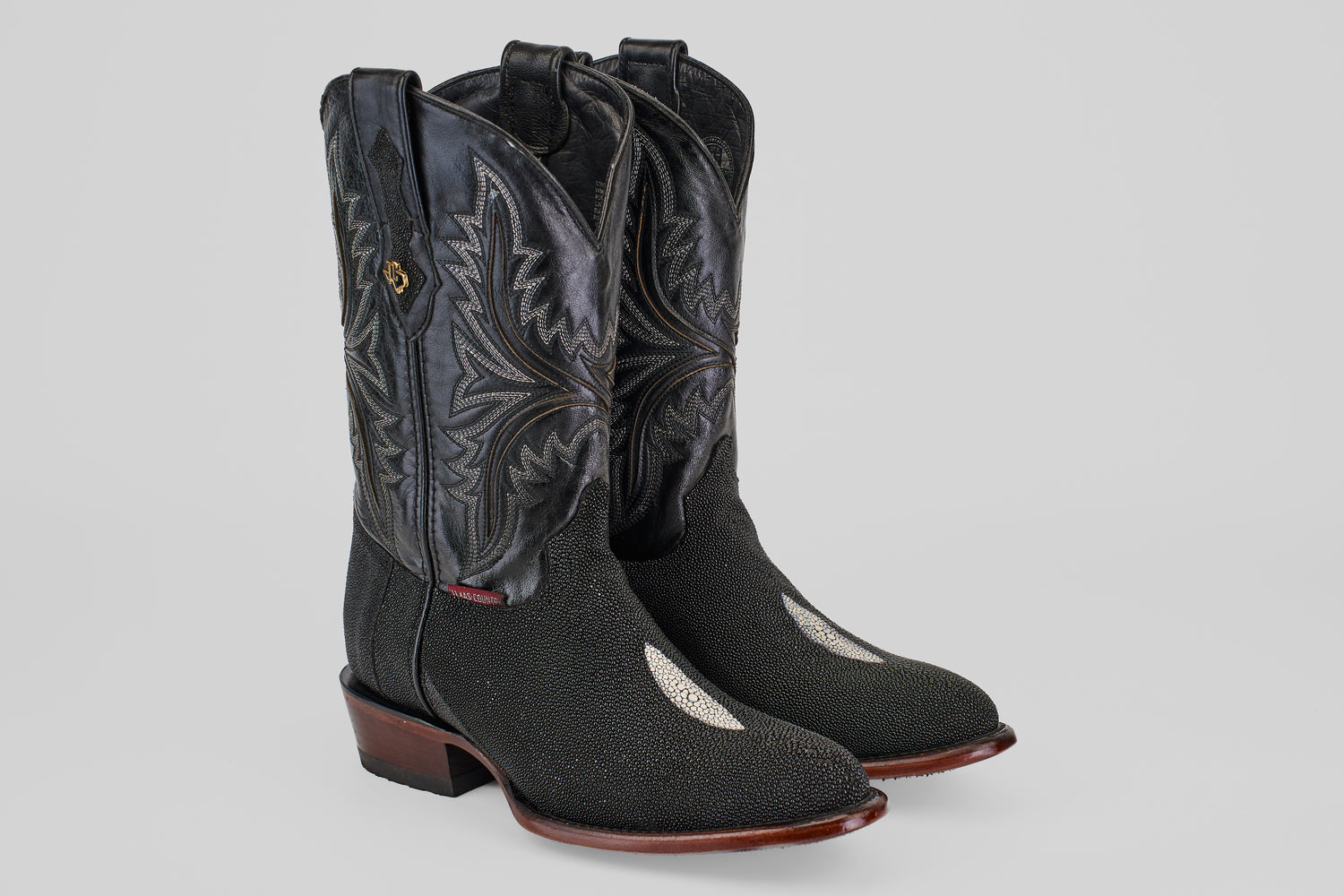 The Ranger – Black – Round Toe men’s cowboy boots feature black stingray leather with decorative stitching, a round toe, dark brown wooden heels and soles, and a distinctive white patch on the top of each foot.
