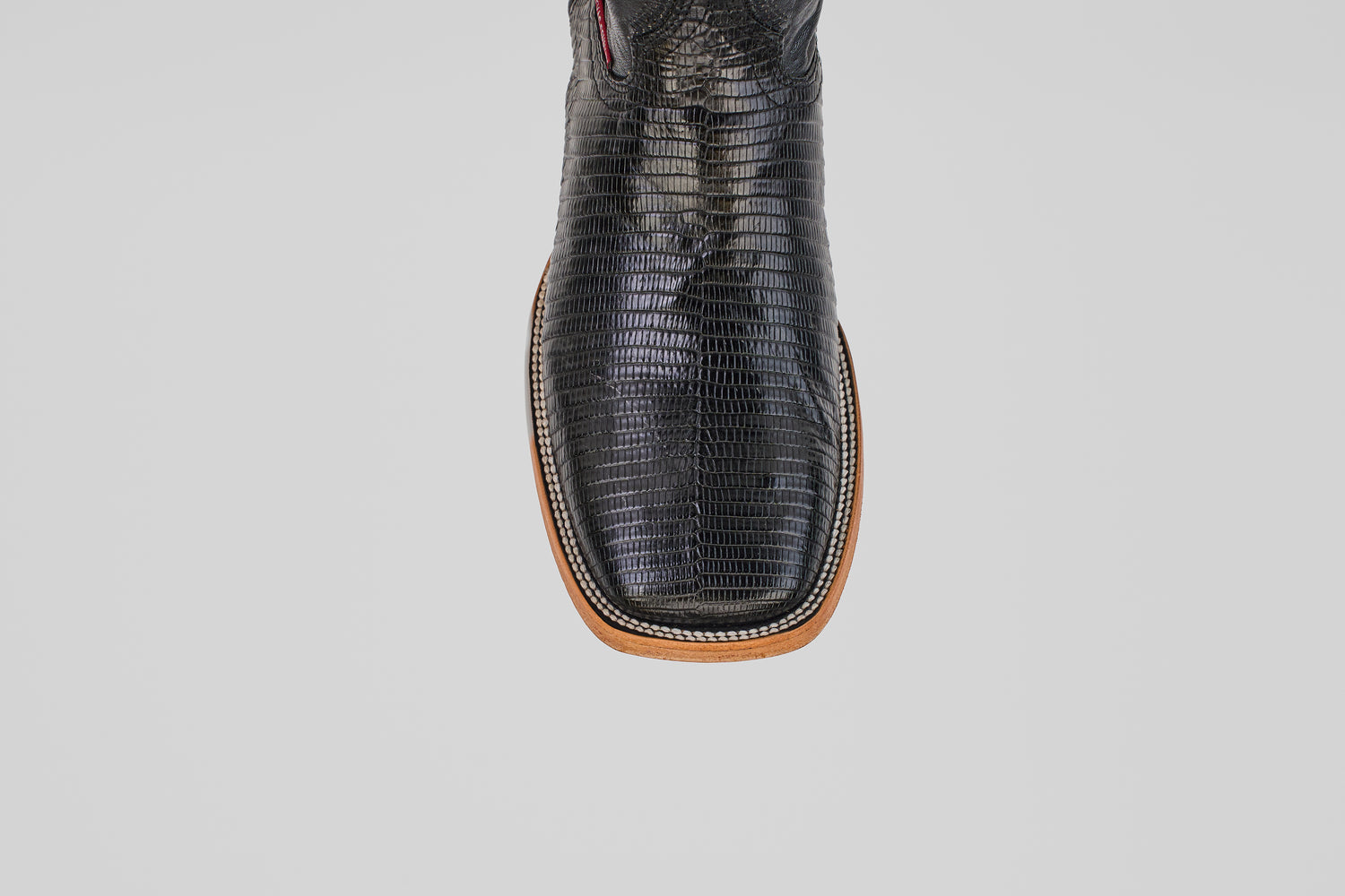 A close-up, top view of the Blaze – Black – Square Toe boots highlights their textured genuine black lizard leather with brown trim, set against a plain light gray background.