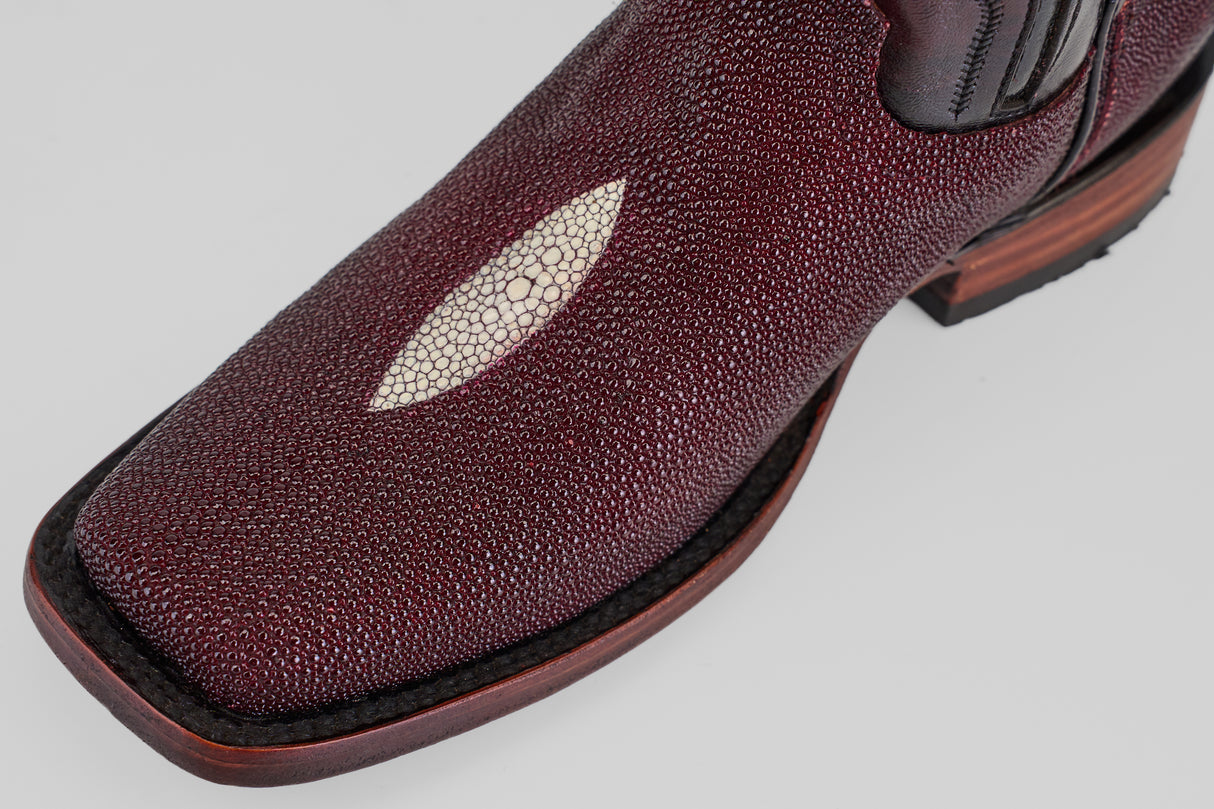 Close-up of the Ranger – Wine – Rodeo Toe cowboy boot, crafted from textured burgundy stingray leather with a white oval inlay on the toe, dark stitching, and a brown wooden heel, set against a light gray background.