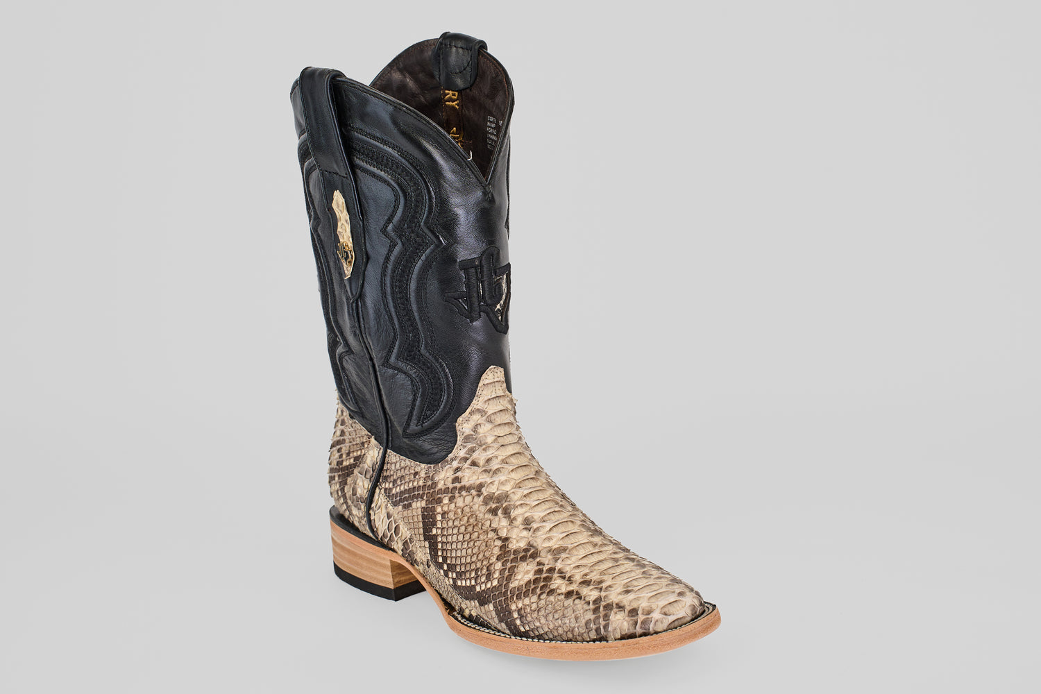 The Tanner - Matte Natural - Square Toe is a cowboy boot with a black upper and tan matte natural python leather lower, decorative stitching, a light wooden heel, and square toe—shown on a plain light gray background.