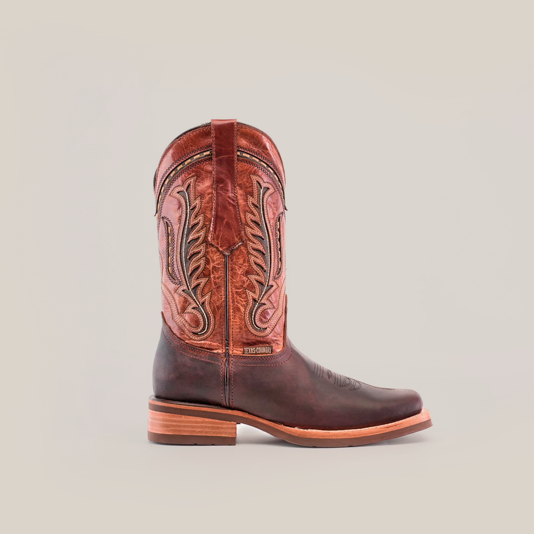 An Azkar Moka Rodeo Toe cowboy boot showcases a brown lower and detailed reddish-brown upper made of premium cowhide. It features a wooden heel and slip-resistant sole, all set against a white background.