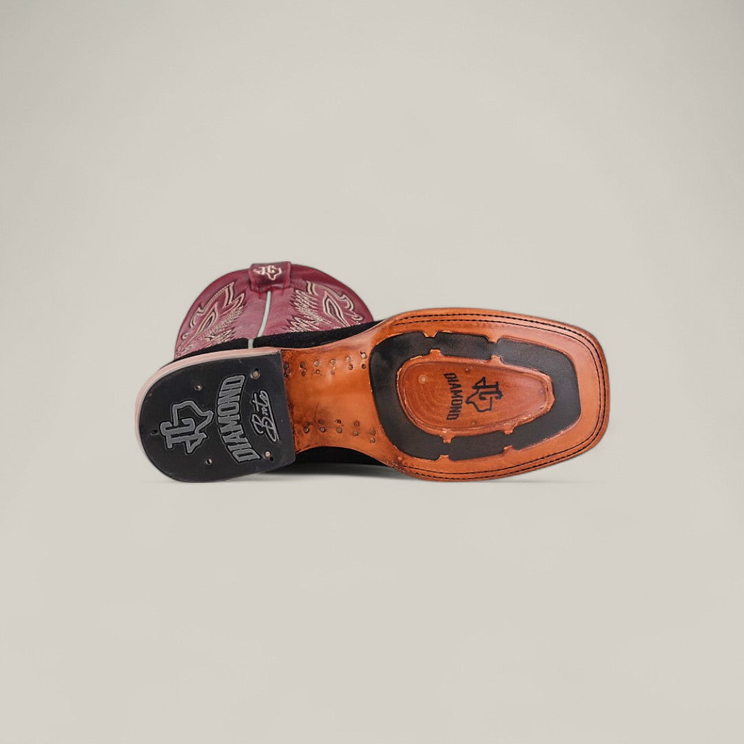 The Colt - Black - Square Toe mens boot is shown on its side with the sole up, highlighting premium suede, detailed stitching, a stamped logo, and a textured tread on the heel for a refined look.