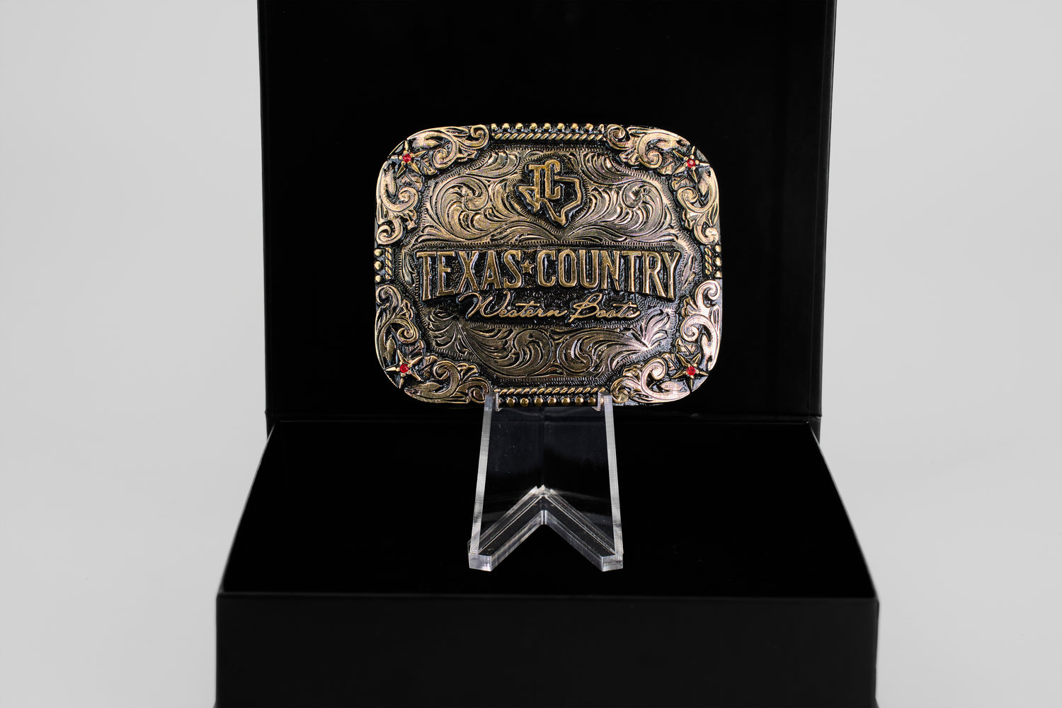 The Texas Country Buckle - Mod 4, a decorative gold and silver Western belt buckle engraved with Texas Country Western Belt, is displayed upright in an open black box—ideal for collectors.