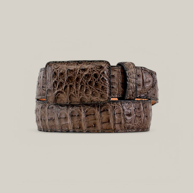 The Exotic Full Quilt Caiman - Serpentine is a rolled-up brown leather belt with a textured crocodile skin pattern, displayed against a light gray background. It features a square buckle and exudes elegance as a luxury accessory.