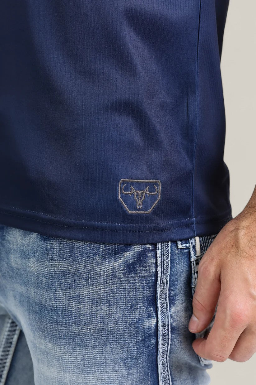 Close-up of a person wearing the Mens Performance Fabric Aztec Panoramic Print Navy Polo (PGP10606) with a bull logo near the hem and light blue distressed jeans; only the torso and hand are shown.