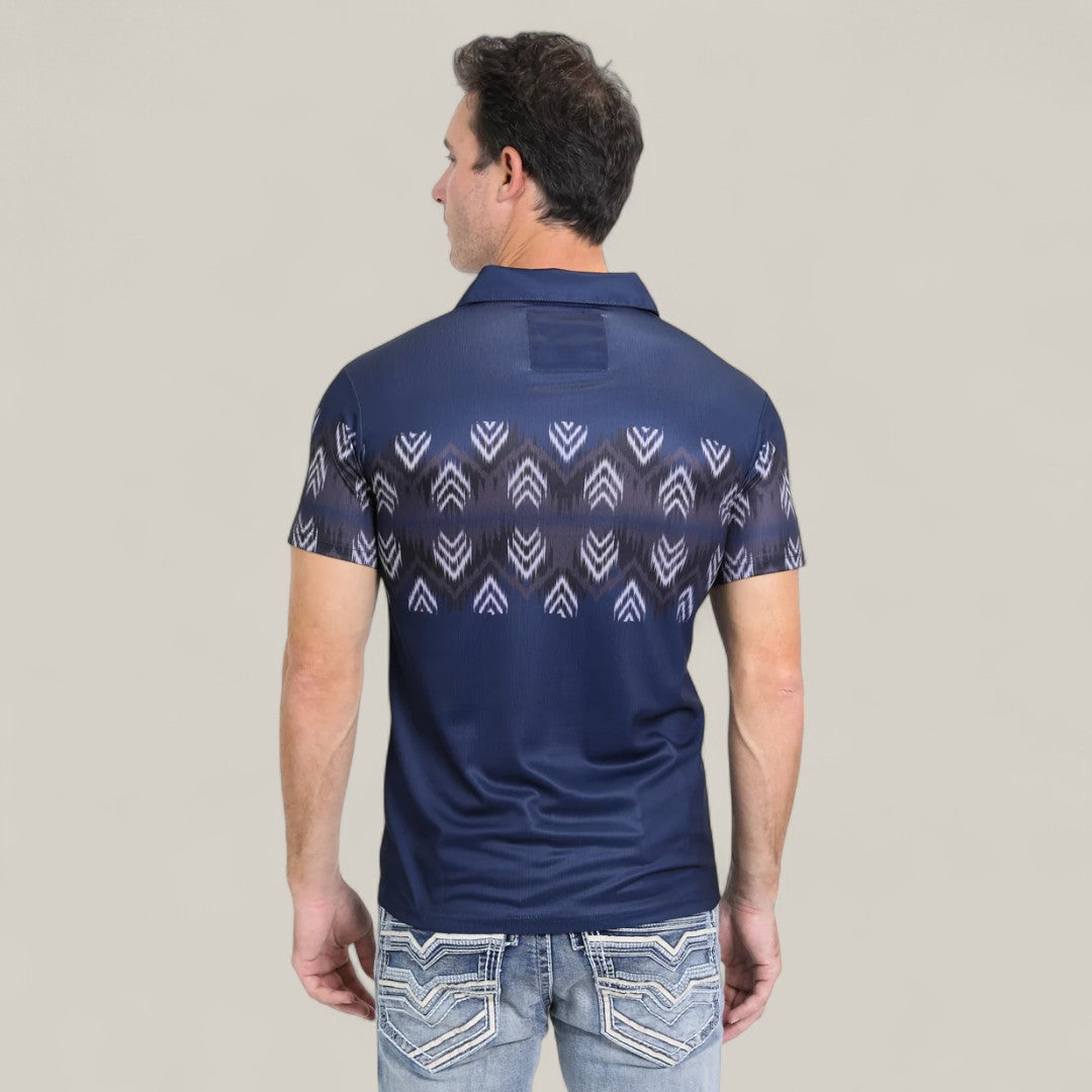 A man faces away in the Mens Performance Fabric Aztec Panoramic Print Navy Polo (PGP10606) featuring a white geometric Aztec design on the back, paired with light blue jeans, set against a plain, light background.
